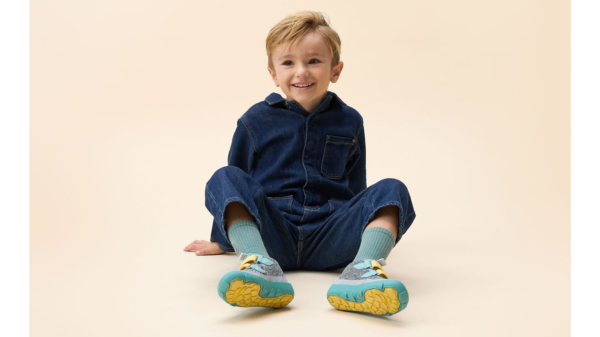 Affenzahn Low Boot Knit Happy - Rhino šedo-zelené zapínáním na suchý zip ve žluté barvě pohled na chlapce sedícího na zemi s pokrčenými nohami detail podrážek a vnitřních stran bot