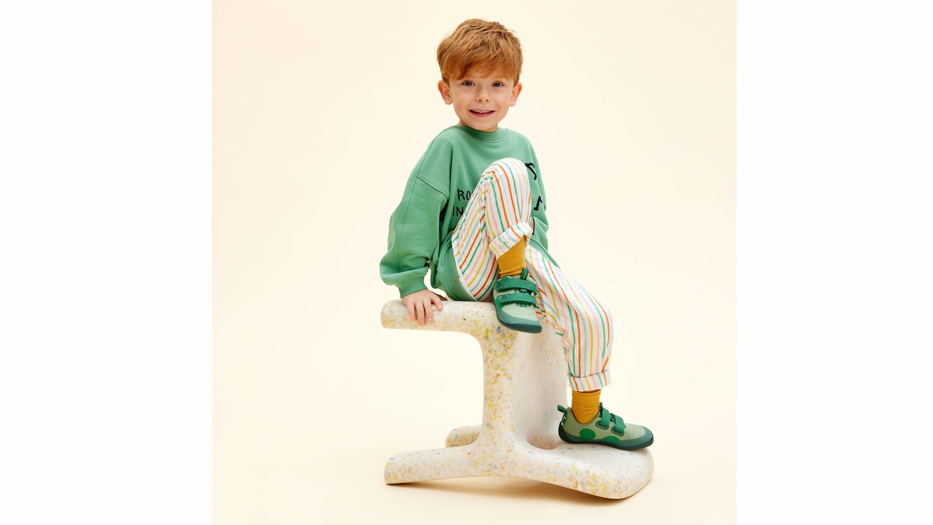 Dítě sedí s botami Affenzahn Sneaker Cotton Lucky - Frog v zelené barvě s flexibilní podrážkou barefoot tenisky.