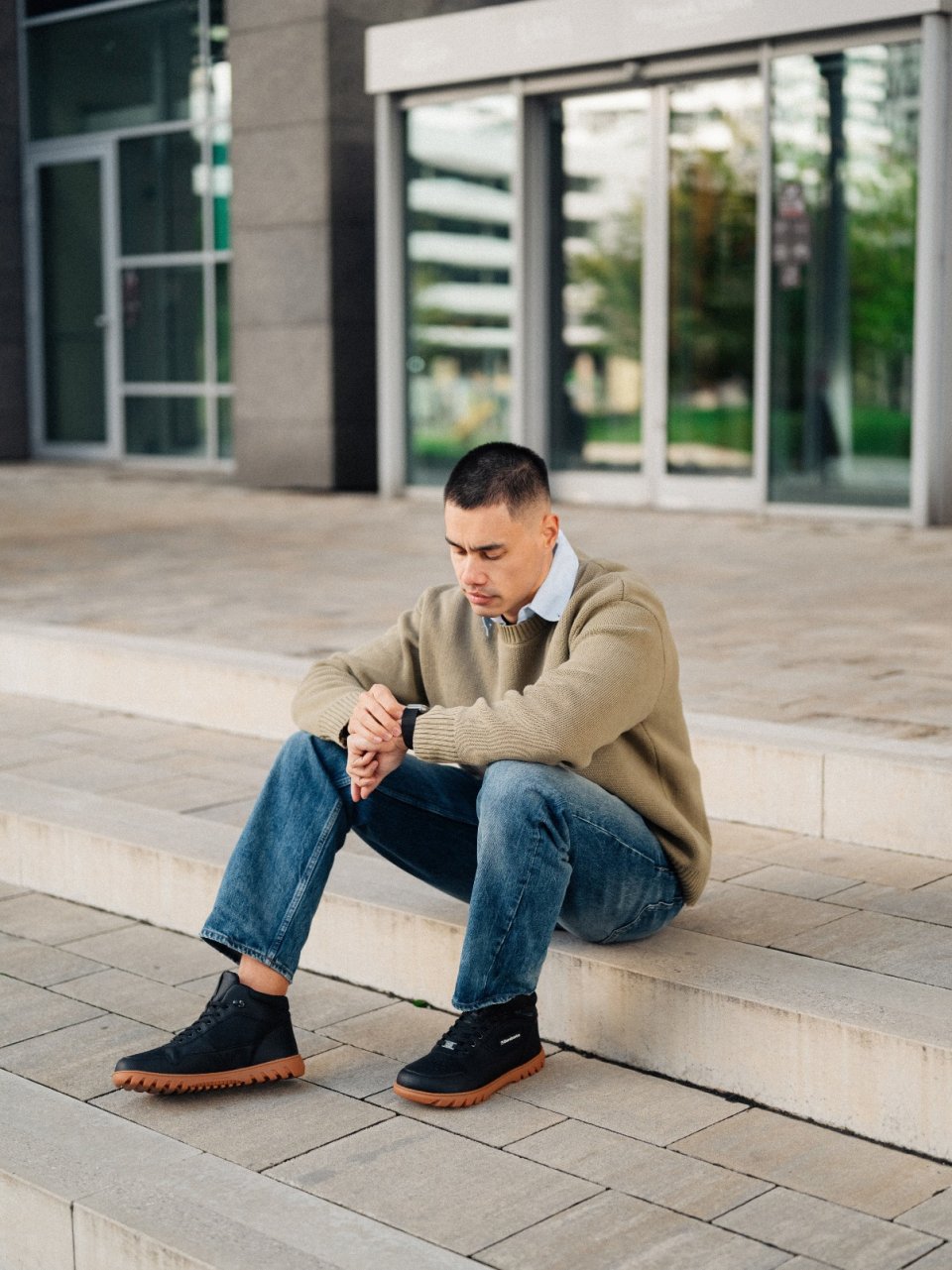 Muž sedí venku na schodech v Barebarics UrbanEdge - Black pánské barefoot botách se širokou špičkou a flexibilní podrážkou.